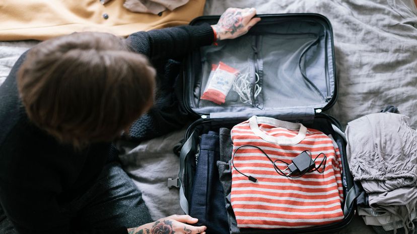 Man packing suitcase. Phone charger is lying on top of clothes.