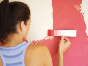 Woman comparing pink paint chips to her pink wall to find a matching color.