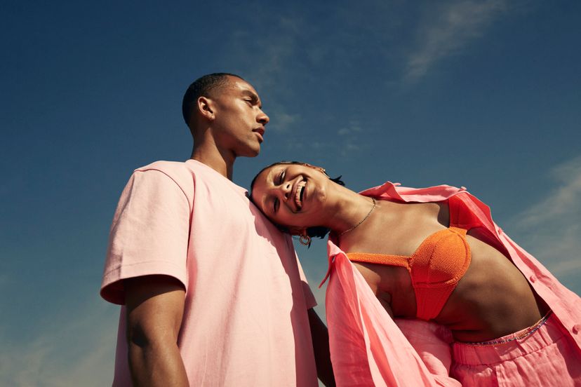 Carefree young woman leaning on male friend while standing against sky