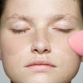 Woman with freckled face covers them with foundation.