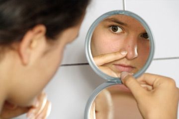 Young teenage female holding a mirror looking at her pimple with concern