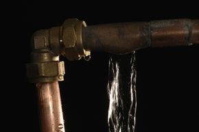 Water pours from two fractures in a copper pipe. Pipe joints are particularly susceptible to leaks but they can happen at any part of the pipe.