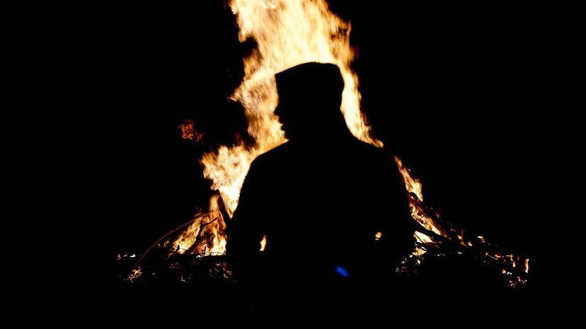 Silhouette figure standing in front of a blazing bonfire
