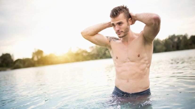 handsome man scruffy shirtless waist deep in water sunset