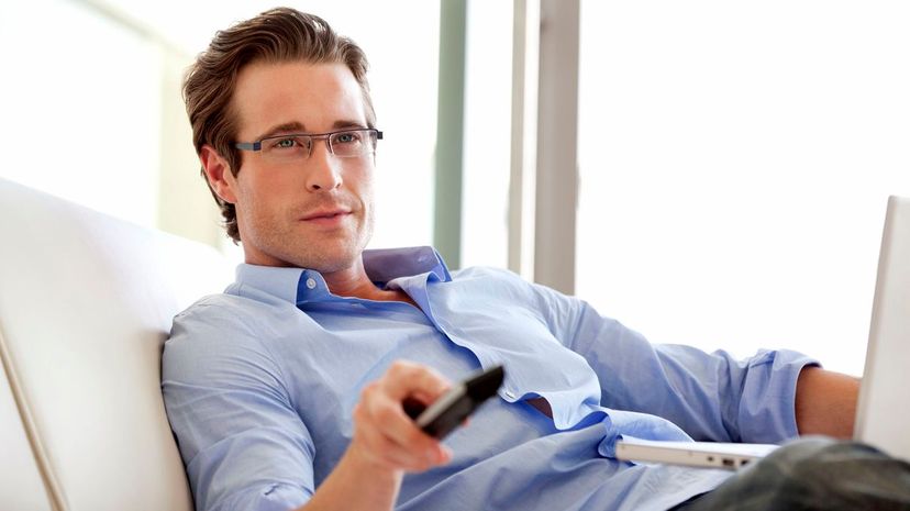 Man sitting with laptop changing channels with remote control