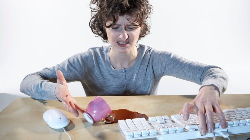 Woman spilling coffee near computer keyboard