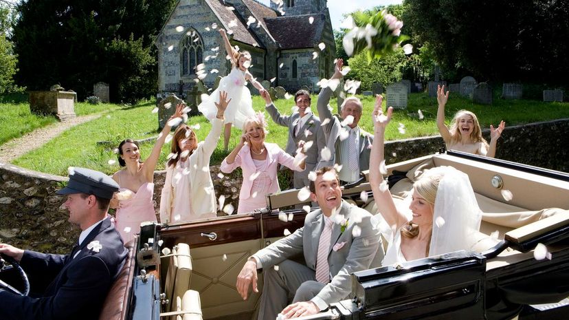 Throwing confetti on bride and groom in convertible vintage car by church