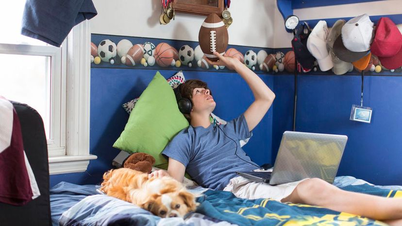 Teenage boy lying on bed with laptop computer, football and dog