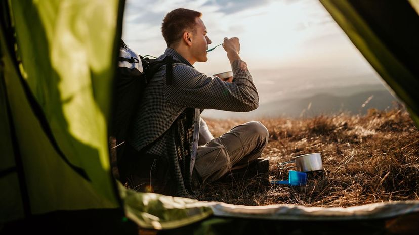 Hiking young man and lunch break in front of his tent