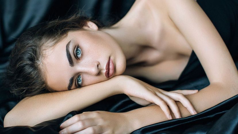 beautiful woman blue eyes laying on side black satin