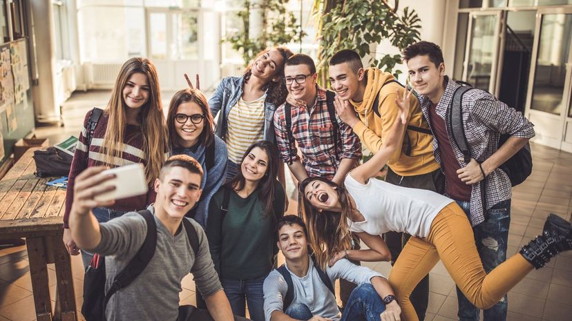 Large group of happy students taking a selfie with cell phone at school