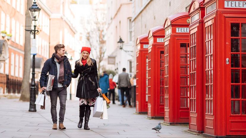 Young shopping couple strolling past red phone boxes, London, UK