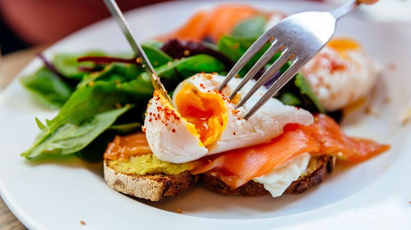 Cutting poached egg on top of avocado toast with salmon