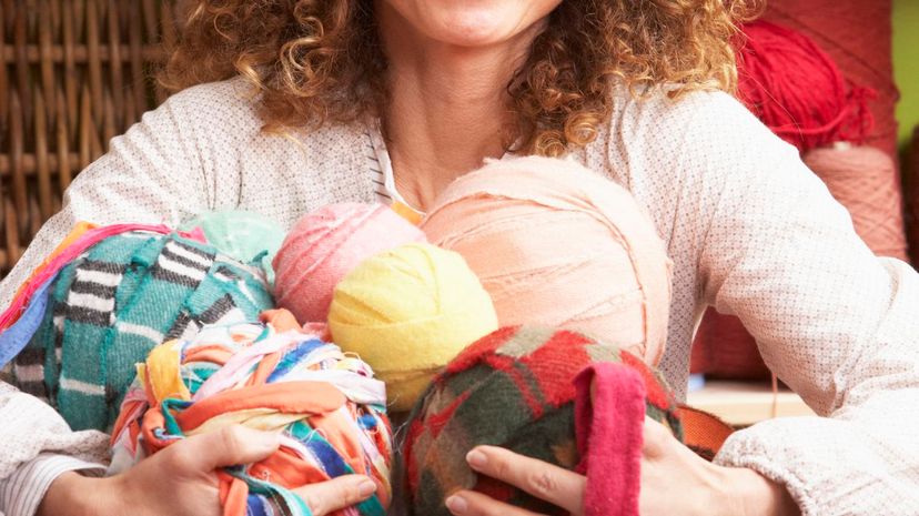 Woman Holding Balls Of Wool Sitting In Front Of Yarn Display