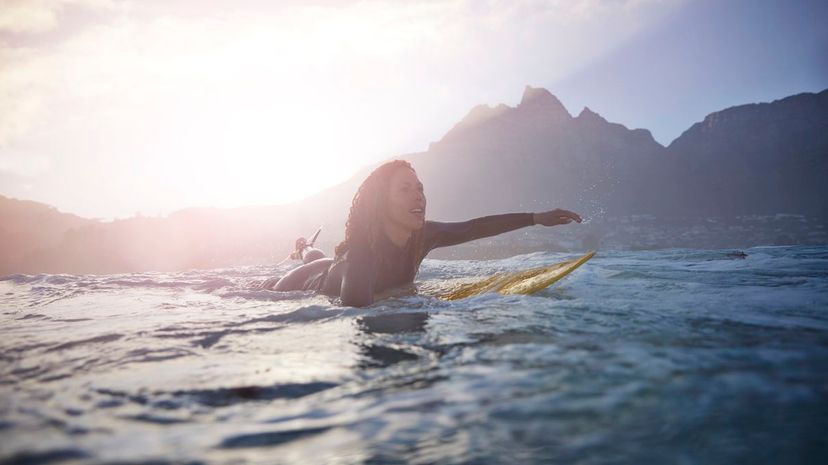 Female surfer paddling at sunrise