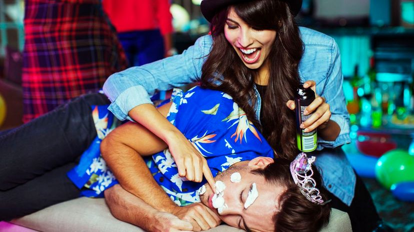 Woman spraying shaving cream on sleeping man's face at party