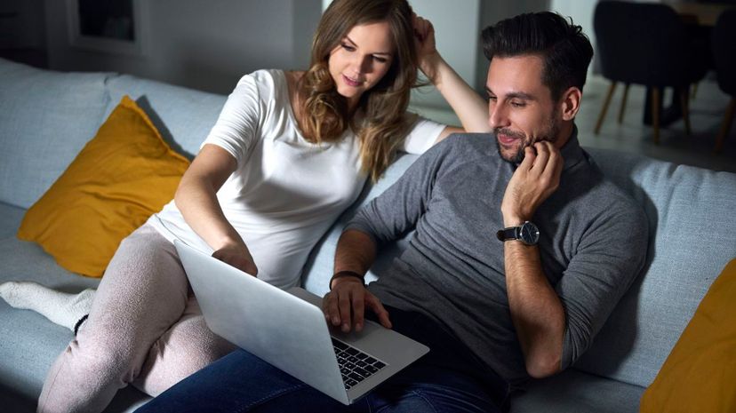 Young couple sitting on sofa in evening looking at laptop