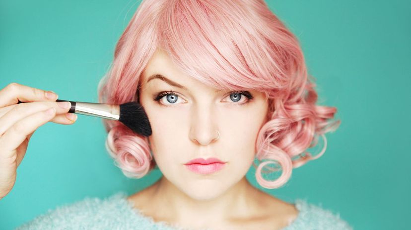 Young woman with pink hair putting on blusher