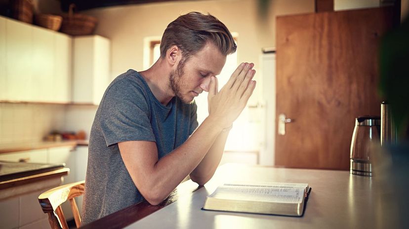 Young man clasping his hands in prayer over an open Bible