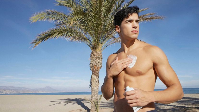 handsome man on beach rubbing suntan lotion dark hair