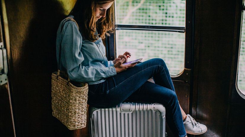 Woman sitting on suitcase in train looking at smart phone