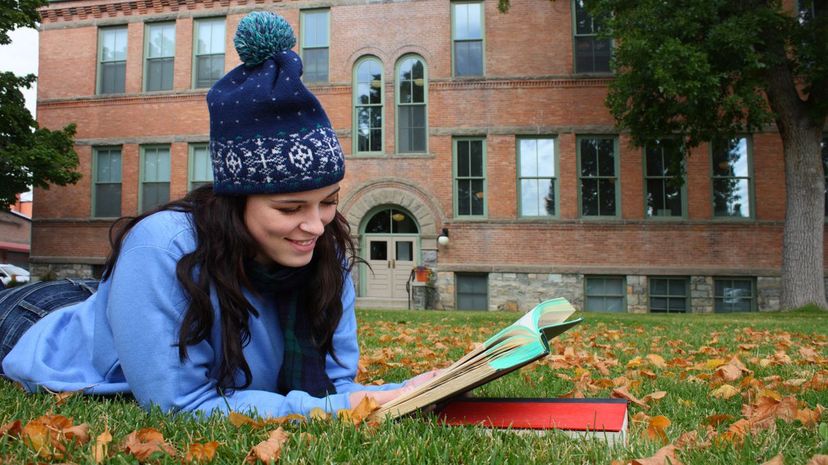 Woman reading book on college campus lawn