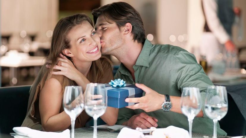 Man kissing and giving gift to woman in restaurant