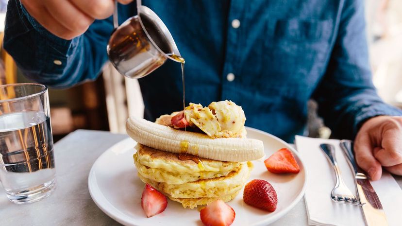 Man pouring maple syrup on pancakes with banana and strawberry