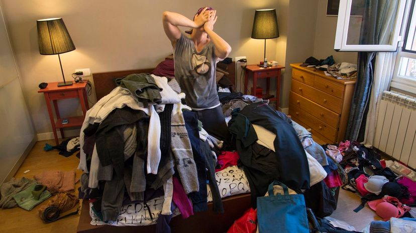 Woman crying among tiles of clothes in a messy bedroom