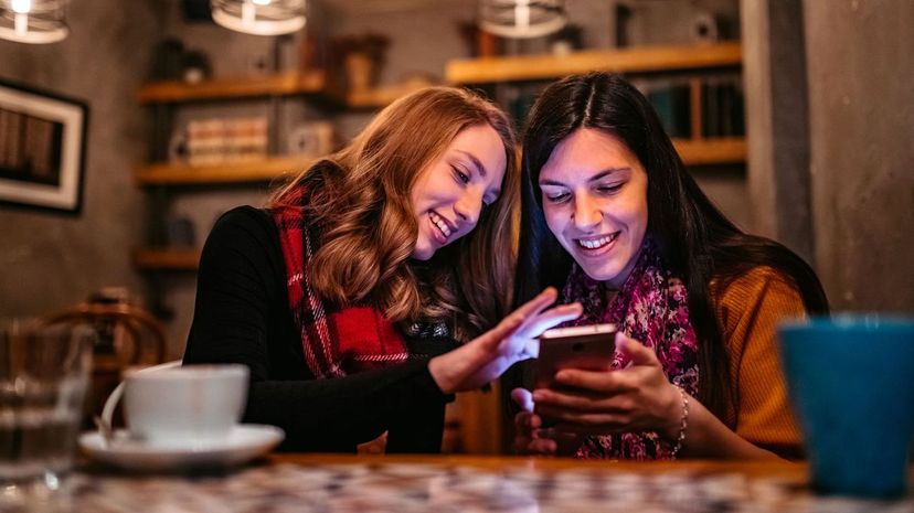 Two female friends using phone on coffee break