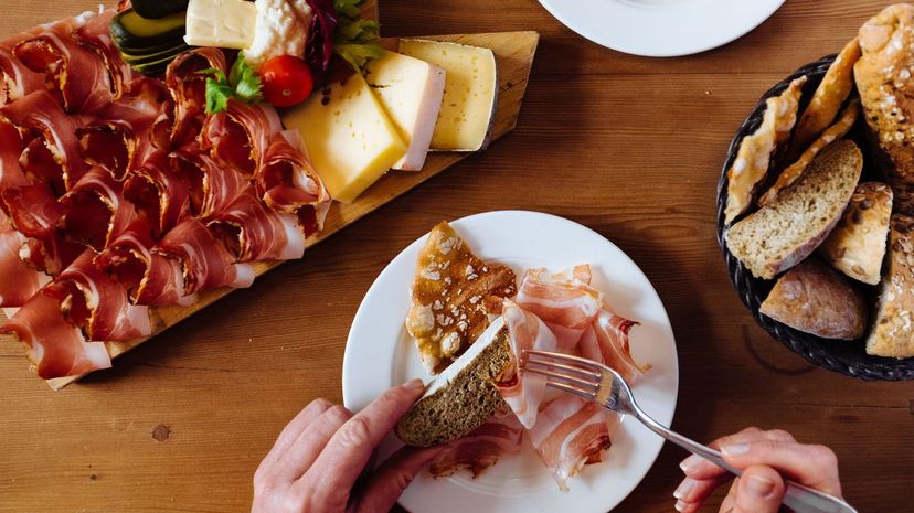 Woman eating variety of bread, cheese and parma ham at table