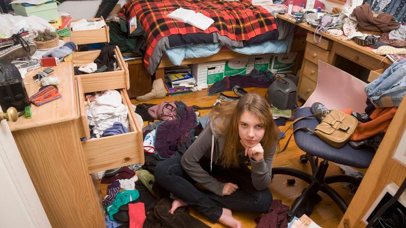 Tenaged girl sitting in messy bedroom