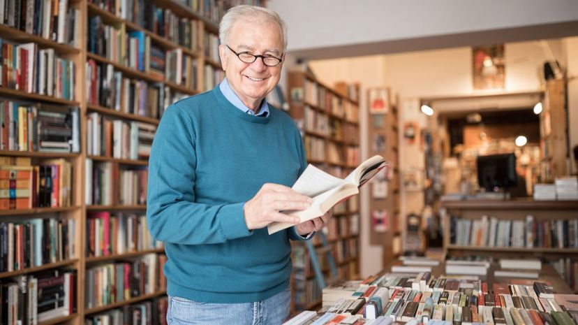 Smiling senior male customer reading book at bookstore