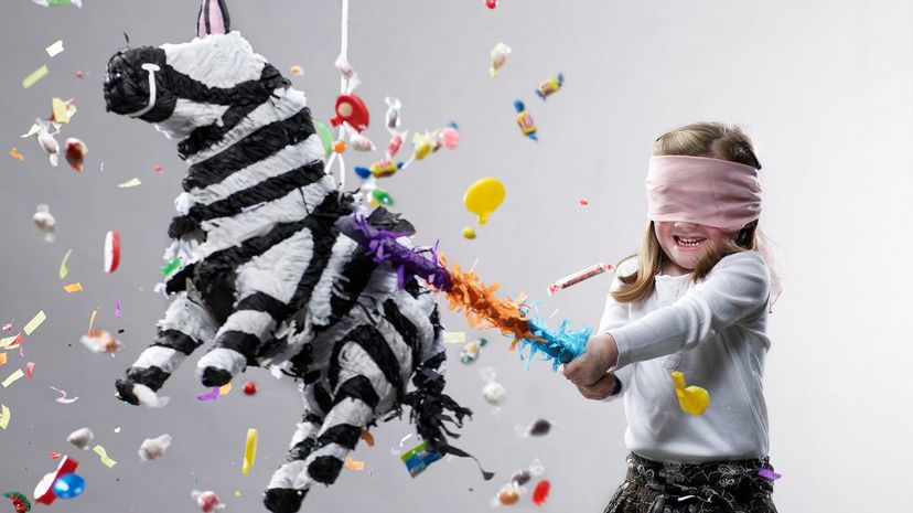 Young girl hitting pinata, candy flying