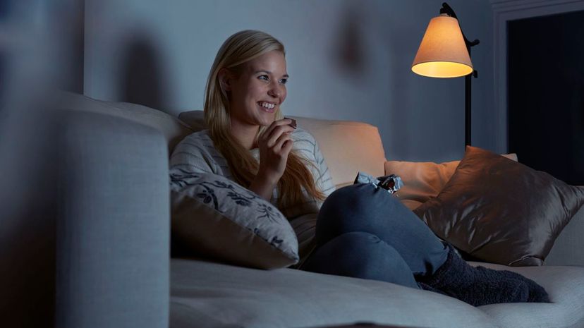 Woman sitting on sofa, watching tv, eating chocolate at night