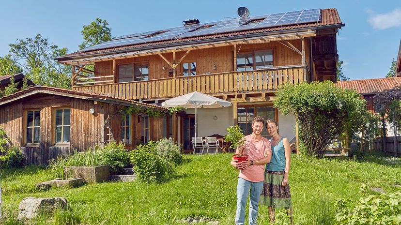 Couple, holding pot plant, standing in front of house with solar panelled roof