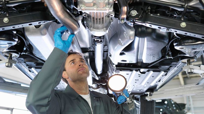 Mechanic working under car in car dealership workshop holding torch