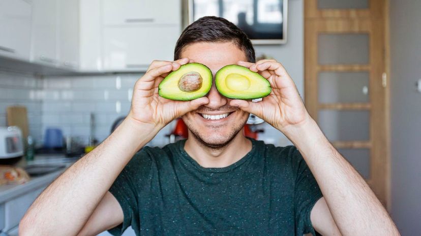 Young man having fun with avocado at the kitchen