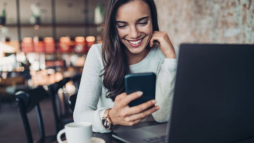 Smiling young woman with laptop and cell phone in cafe