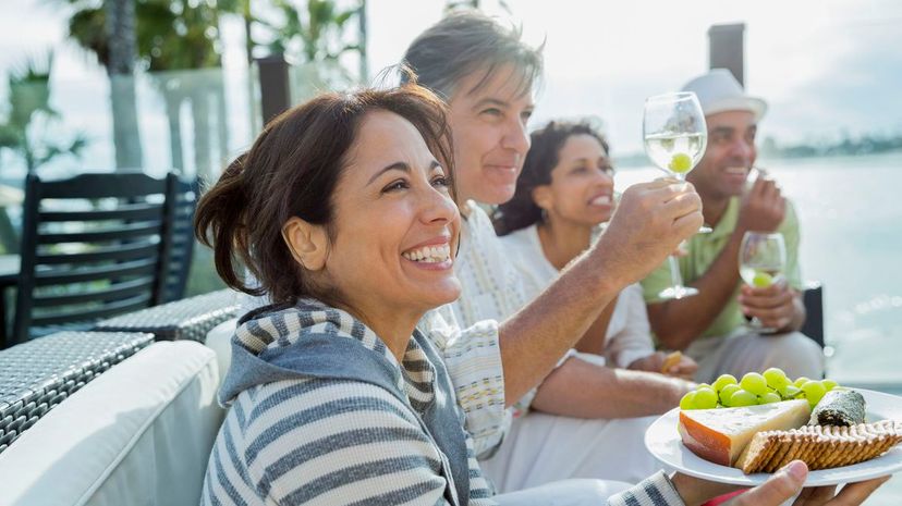 Smiling mature woman holding cheese plate with friends on patio