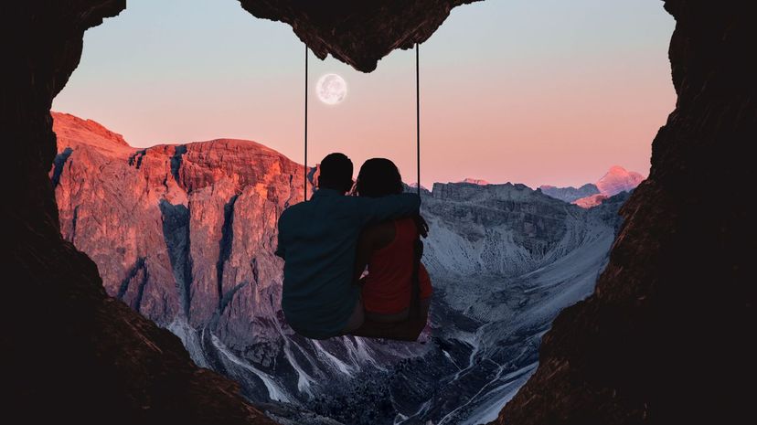 Couple on swing contemplating the mountains in a romantic view with heart shape