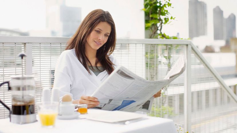 Woman reading newspaper and having breakfast on balcony