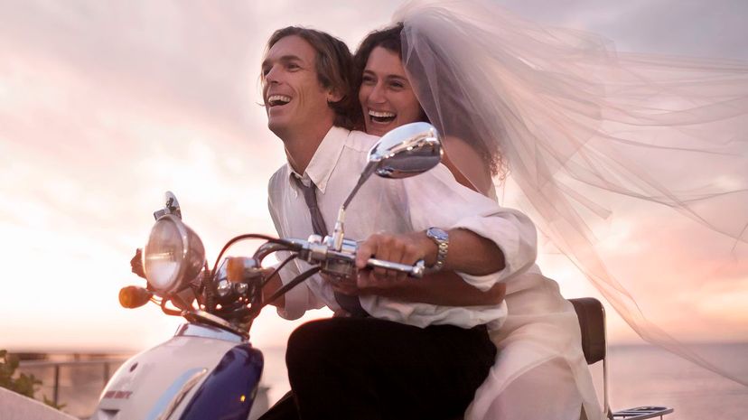 Bride and groom riding motorcycle on beach against sunset