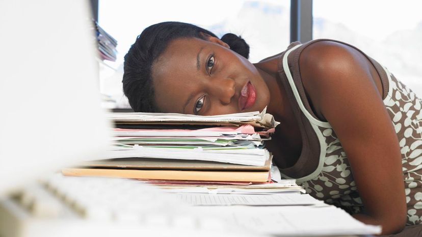 Young woman leaning head on pile of files on desk