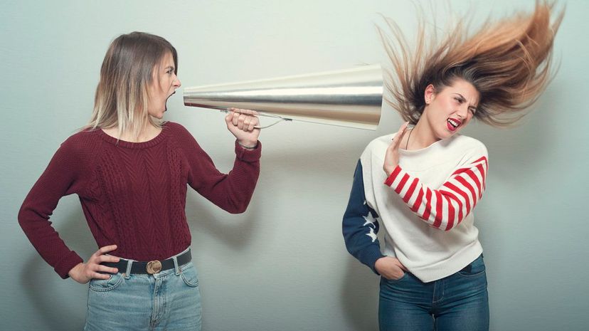 Angry young woman shouts with megaphone to another woman