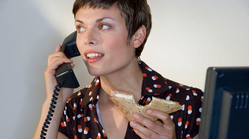 Businesswoman eating sandwich, using telephone, smiling