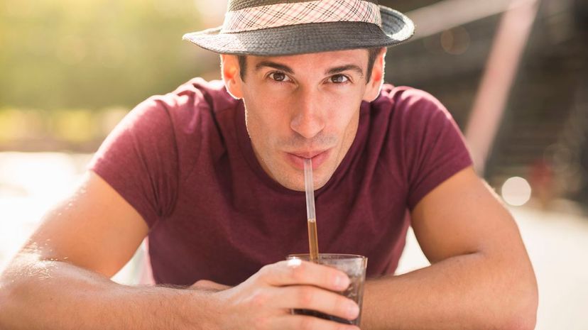 Young man wearing hat drinking through straw