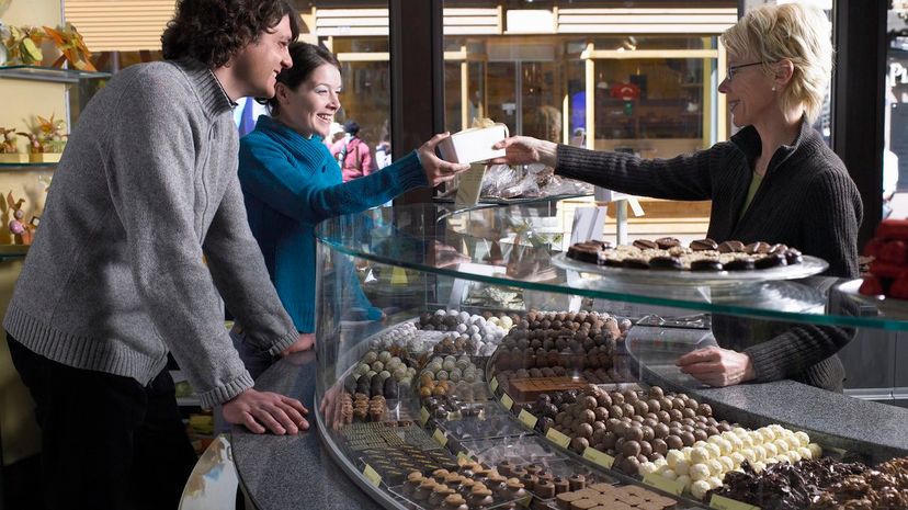 Woman handing couple box across counter in chocolate shop
