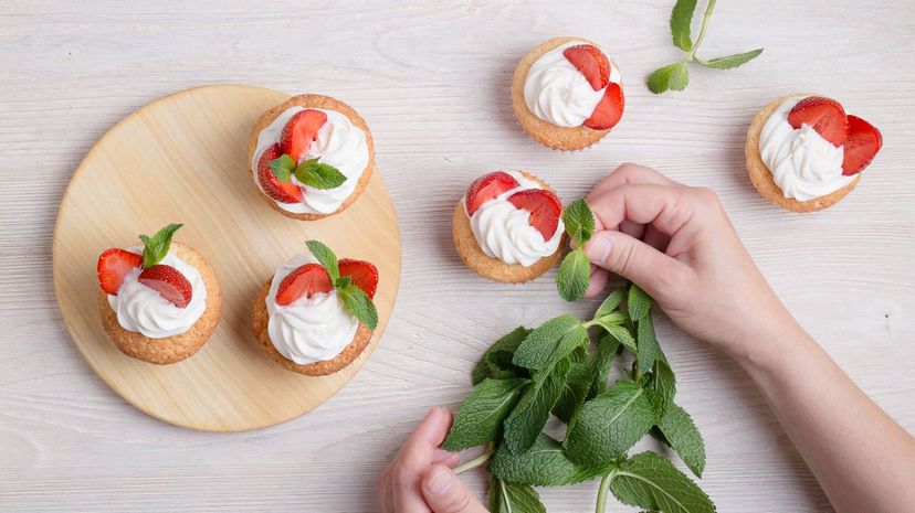 Placing mint leaf on the top of a buttercream cupcake with strawberries