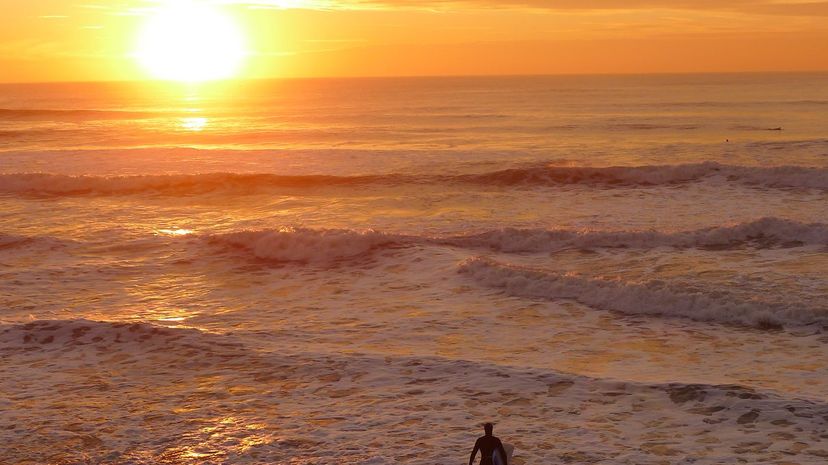A surfer heading out from San Francisco's Ocean Beach at sunset